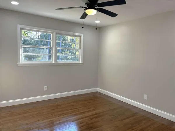 an empty room with wooden floor fan and windows