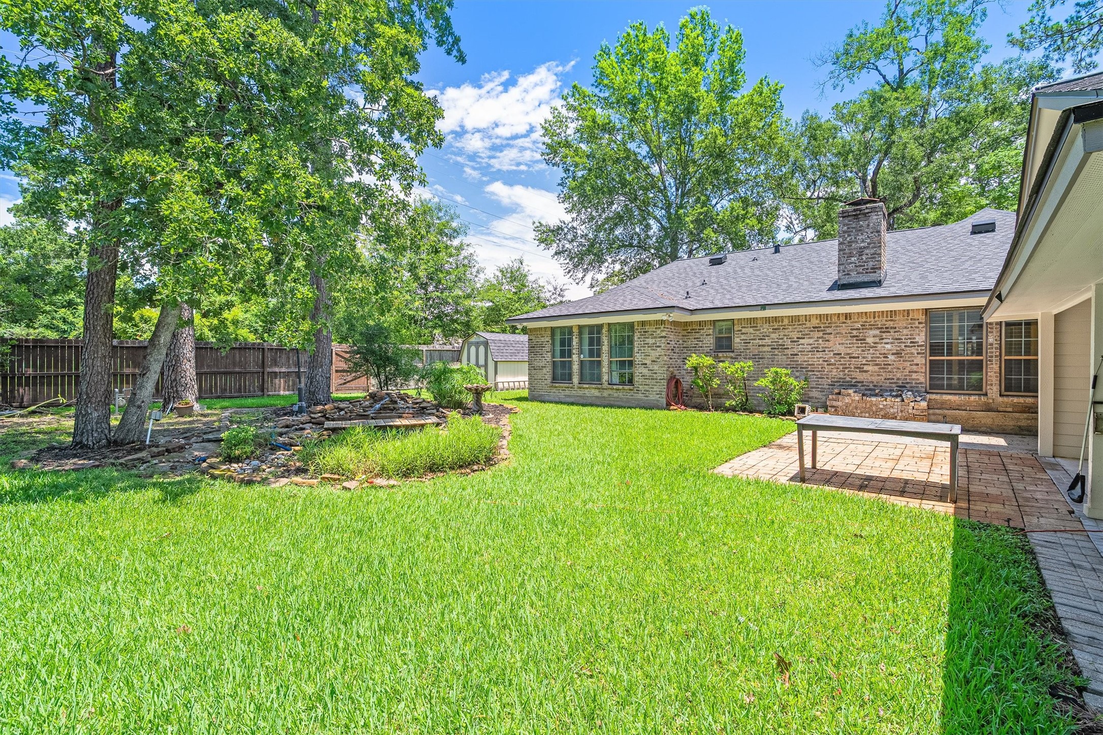 826 North Rivershire Drive Conroe, TX 77304 - Photo 35 of 46 This angle shows the full scale of the backyard. Mature trees, lush lawn, fully fenced, storage shed, and that koi pond tucked in the corner under the canopy. There is a lot going on back here in the best possible way