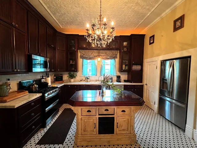 a kitchen with stainless steel appliances granite countertop a refrigerator a sink dishwasher a stove and a dining table with wooden floor