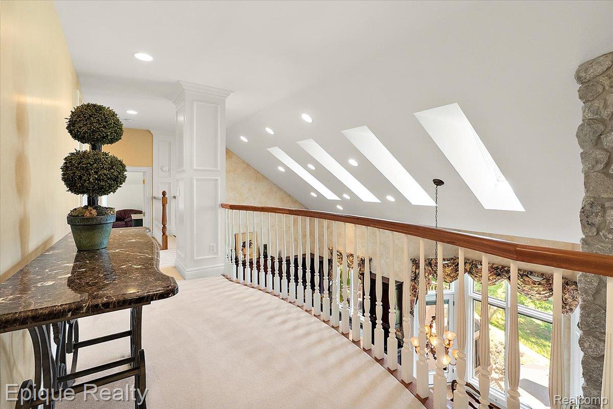 7662 Devins Ridge Clarkston, MI 48348 - Photo 56 of 81 Upper-level hallway featuring a curved railing with turned spindles, a stone accent column, and multiple skylights
