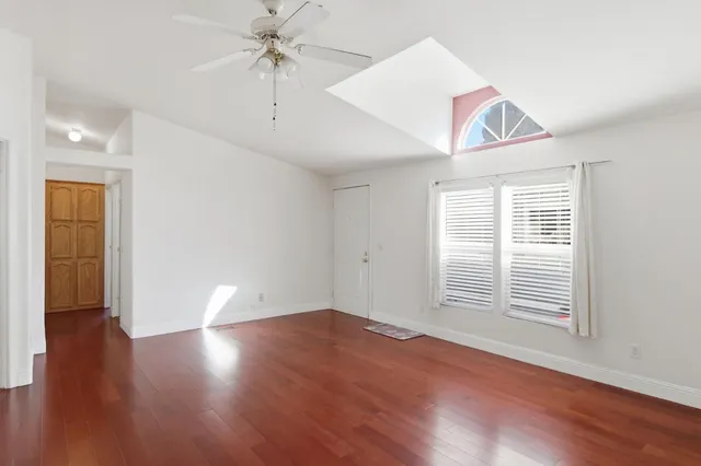 an empty room with wooden floor chandelier fan and windows