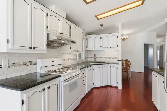 a kitchen with stainless steel appliances granite countertop a stove a sink and white cabinets