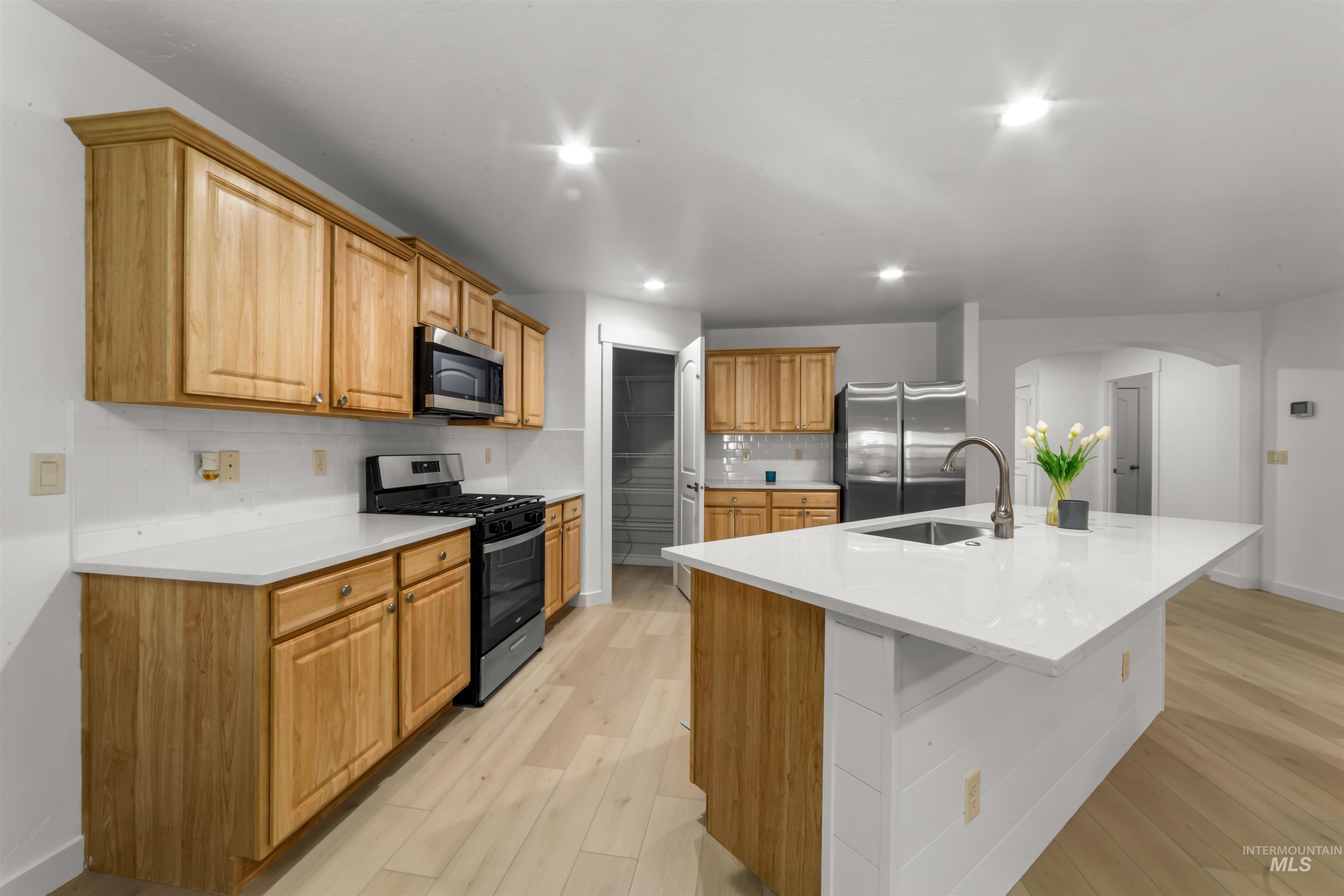 548 North Ripplerock Place Star, ID 83669 - Photo 20 of 42 Kitchen featuring stainless steel appliances, an island with sink, arched walkways, decorative backsplash, and light wood-style flooring