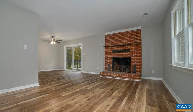 a view of an empty room with wooden floor fireplace and a window