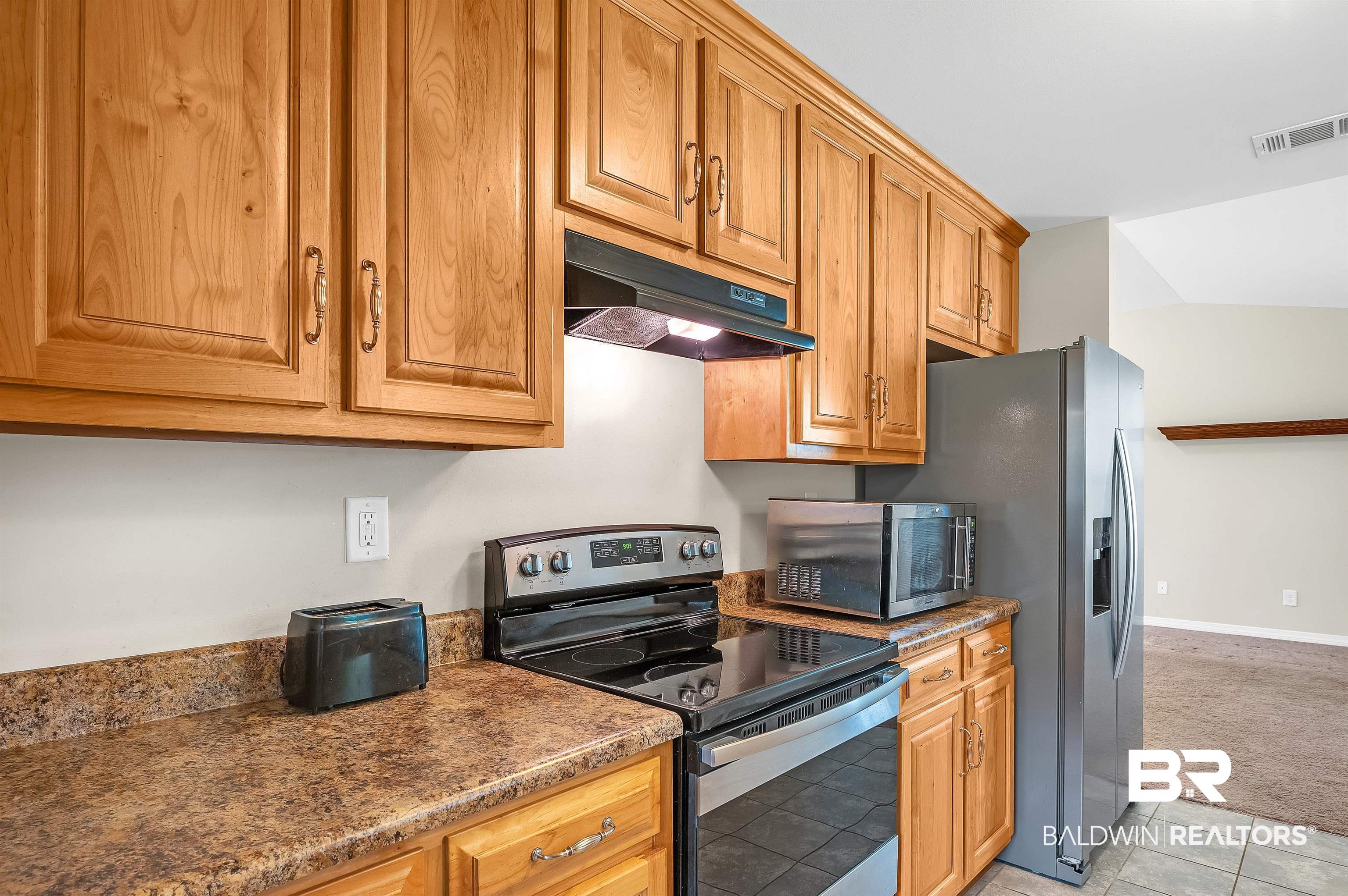 22810 Ard Road Robertsdale, AL 36567 - Photo 34 of 65 Kitchen featuring under cabinet range hood, appliances with stainless steel finishes, light carpet, light tile patterned floors, and brown cabinets