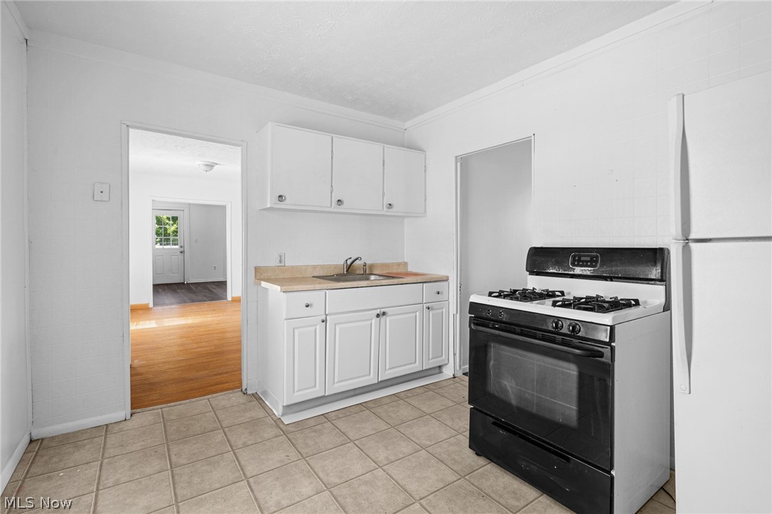 2387 29th Street Southwest Akron, OH 44314 - Photo 22 of 24 Kitchen featuring gas stove, freestanding refrigerator, light countertops, white cabinets, and crown molding