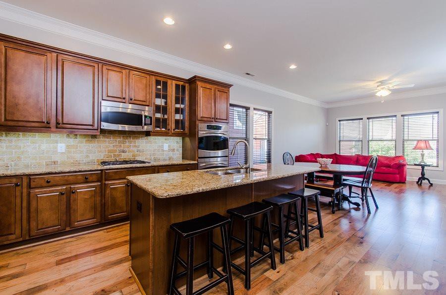 1407 Van Page Boulevard Raleigh, NC 27607 - Photo 8 of 25 a kitchen with stainless steel appliances granite countertop a stove top oven a sink dishwasher a dining table and chairs with wooden floor