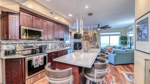 a kitchen with stainless steel appliances granite countertop a refrigerator a sink dishwasher a stove and a dining table with wooden floor