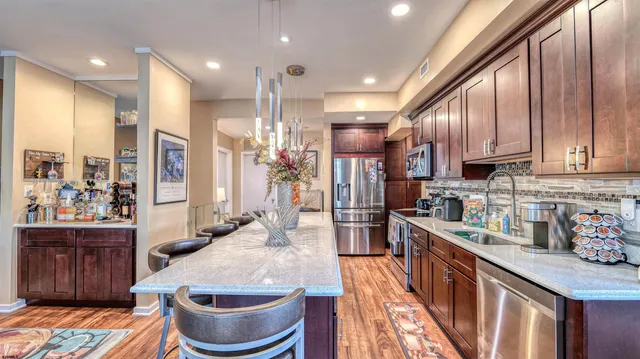 a kitchen with stainless steel appliances granite countertop a refrigerator a sink dishwasher a stove and a dining table with wooden floor