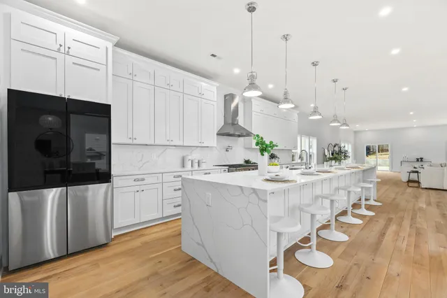 a large kitchen with kitchen island granite countertop a stove a sink a refrigerator and white cabinets with wooden floor