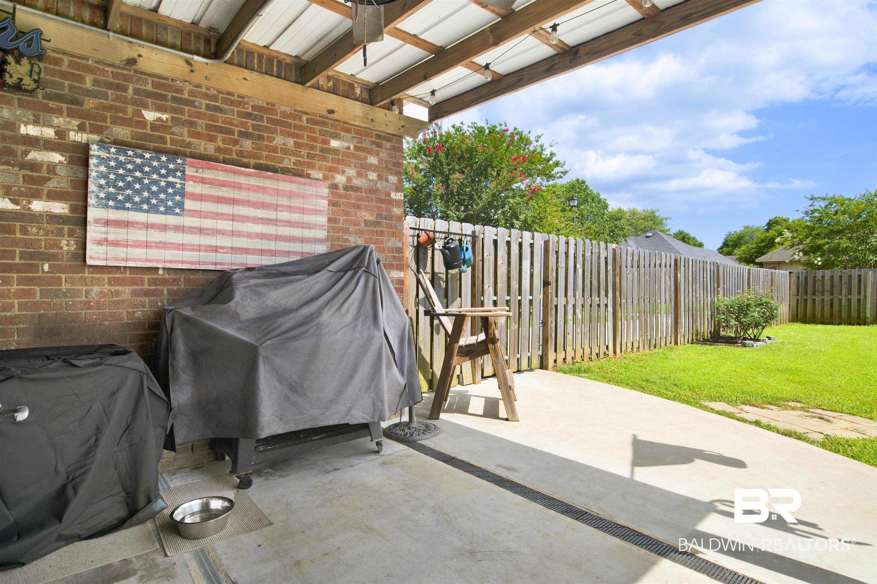 10368 Gayfer Rd Extension Fairhope, AL 36532 - Photo 33 of 43 Covered patio featuring a brick exterior wall, concrete flooring with drainage, and a wooden privacy fence enclosing a grassy yard