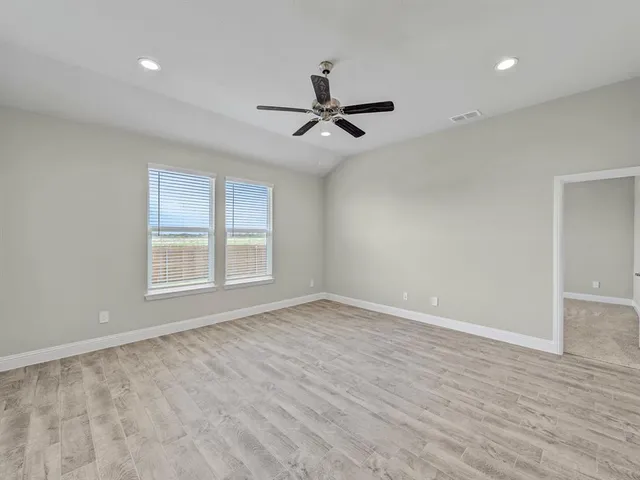an empty room with wooden floor ceiling fan and windows