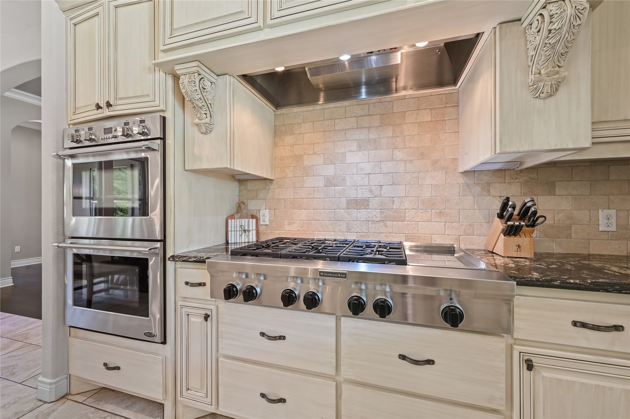 387 Corral Road Smithville, TX 78957 - Photo 14 of 40 Gourmet kitchen featuring a stainless steel gas range, coordinating stainless steel double wall ovens, granite countertops, an exposed brick backsplash, and custom cabinetry with decorative corbels