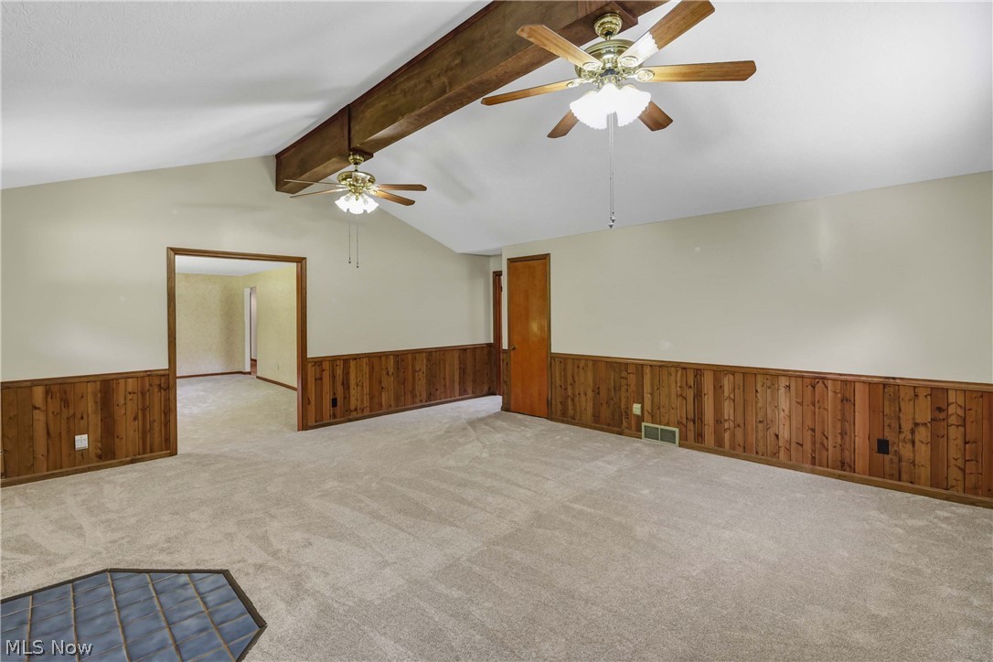 301 Crosse Road Amherst, OH 44001 - Photo 18 of 49 Living area featuring vaulted ceilings with exposed wood beams, wood paneling, light-toned carpeting, and two ceiling fans with integrated lighting