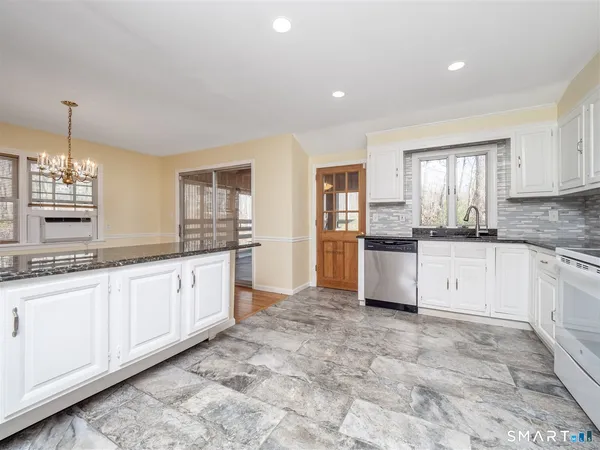 a large kitchen with granite countertop a stove a sink dishwasher a refrigerator and white cabinets with wooden floor