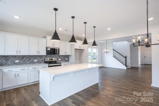 a kitchen with stainless steel appliances kitchen island granite countertop a stove a sink and white cabinets with wooden floor