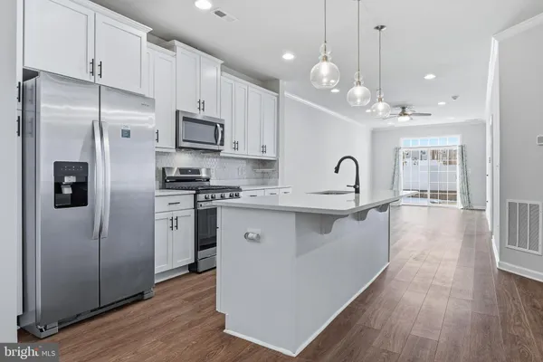 a kitchen with stainless steel appliances granite countertop a refrigerator a sink dishwasher a stove and white countertops with wooden floor