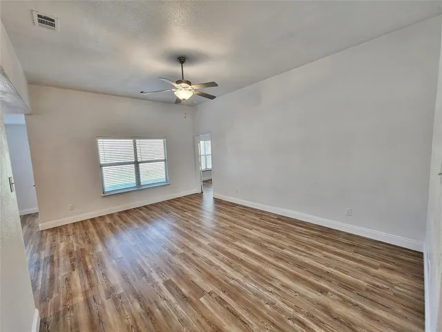 an empty room with wooden floor chandelier fan and windows
