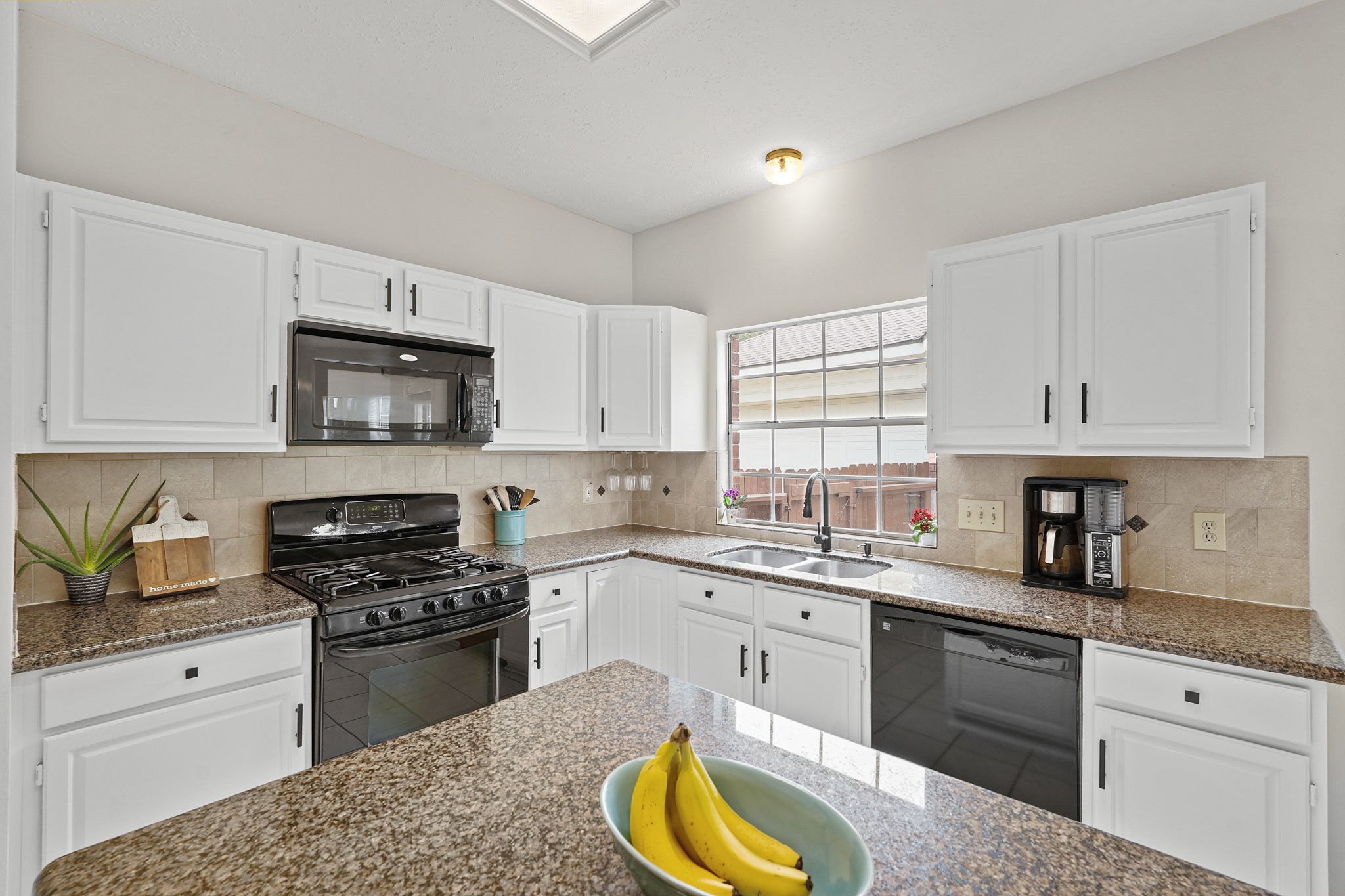 16114 Kintyre Point Road Houston, TX 77095 - Photo 22 of 44 This bright kitchen features white cabinetry, granite countertops, and modern appliances, including a gas stove and built-in microwave. Natural light pours in through a large window, highlighting the spacious, functional layout.