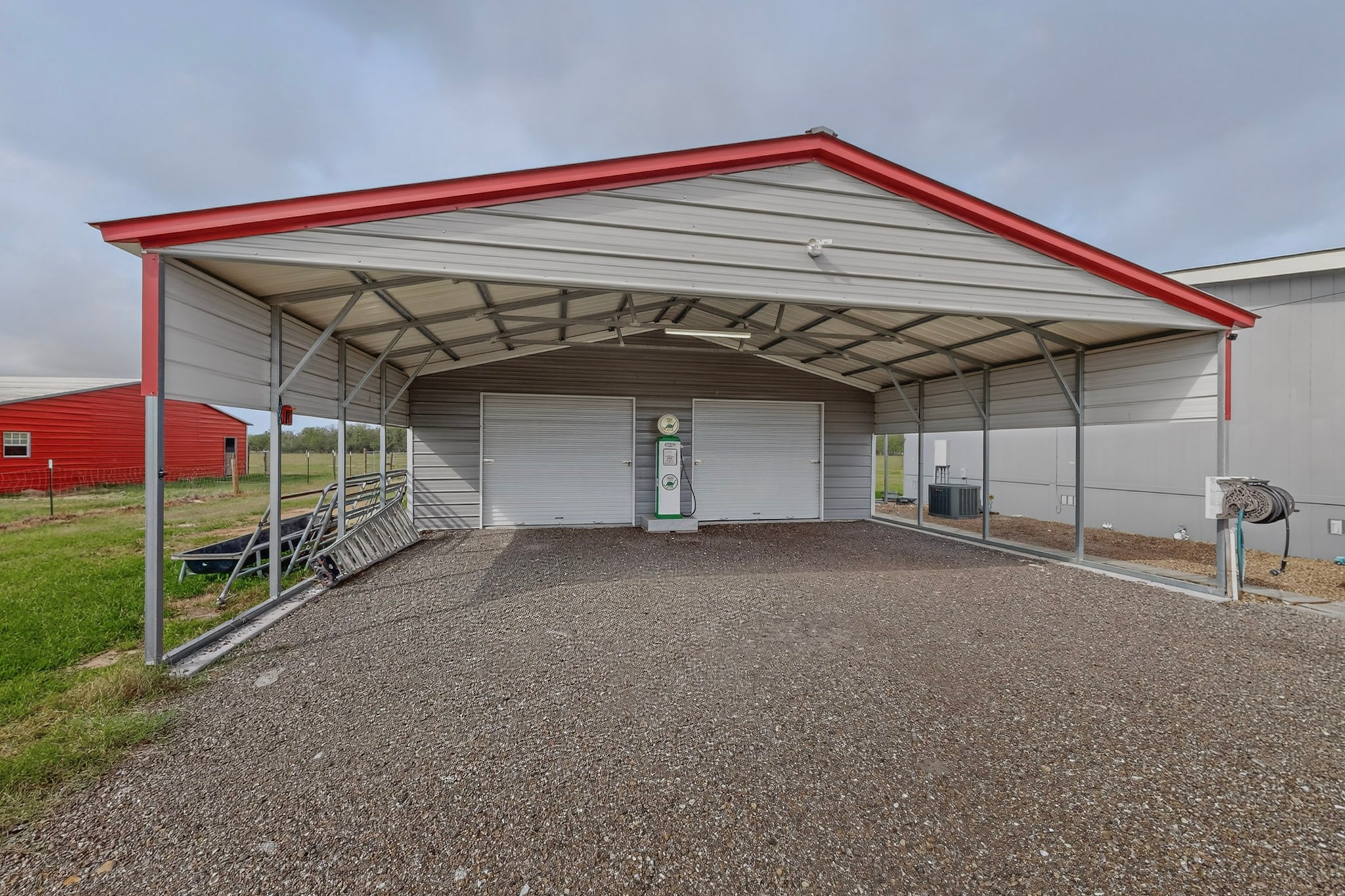 664 Garrett Road Yoakum, TX 77995 - Photo 12 of 39 Gray metal carport with a red trim roof, featuring a gravel ground surface and two garage doors