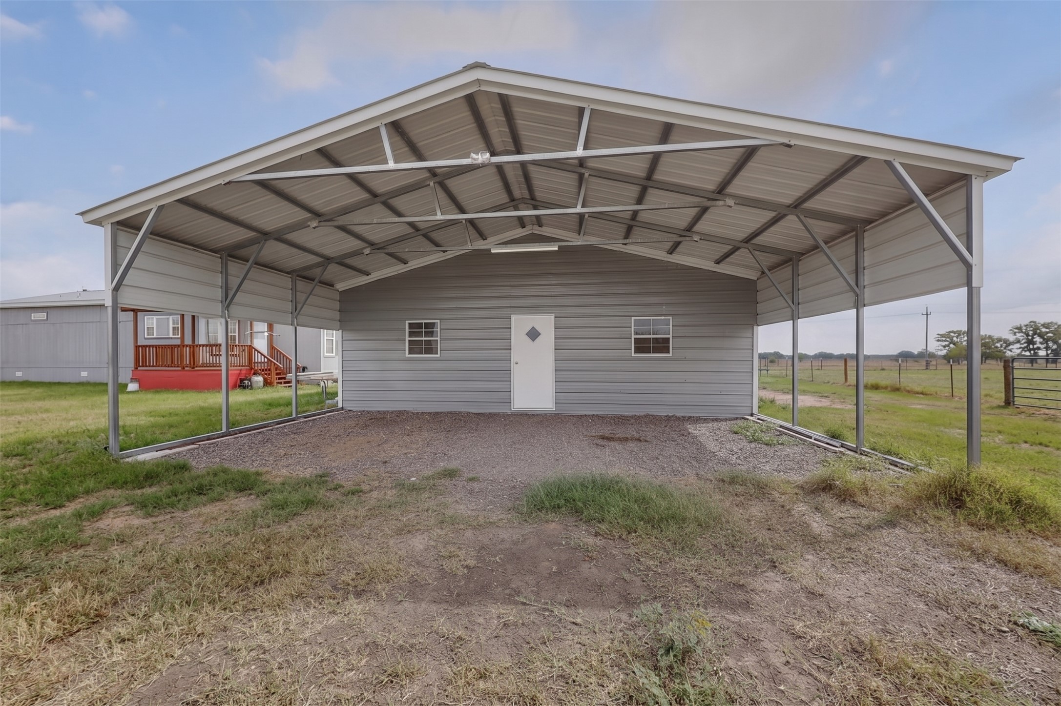 664 Garrett Road Yoakum, TX 77995 - Photo 14 of 39 Metal carport structure featuring a light gray exterior, white entry door with a decorative window, and two double-hung windows