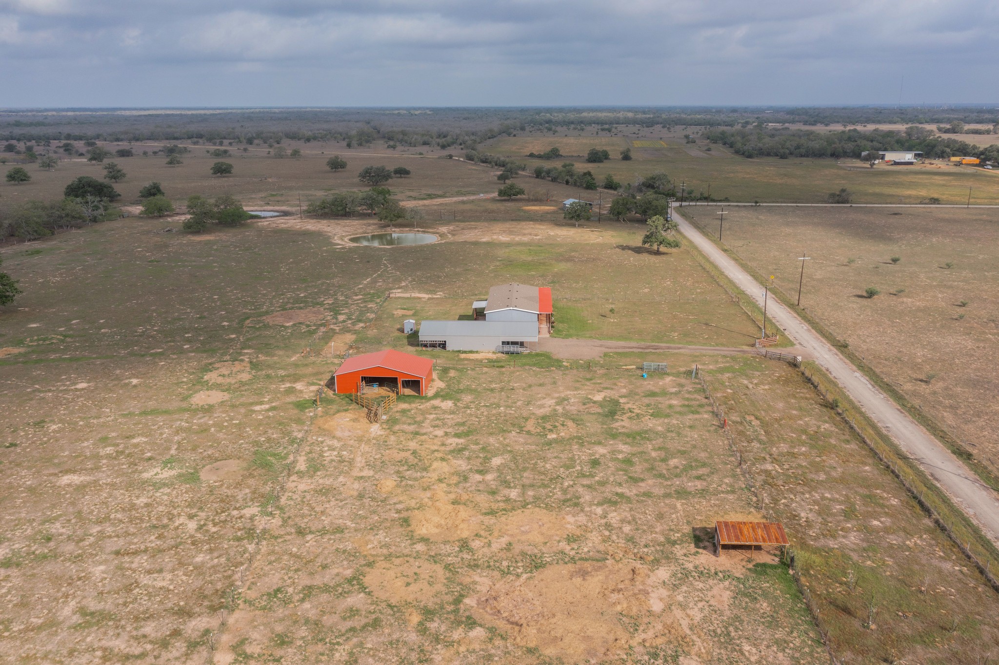 664 Garrett Road Yoakum, TX 77995 - Photo 25 of 39 Expansive rural property featuring an orange-roofed barn, a silver-roofed main structure, a pond, and a lengthy unpaved road