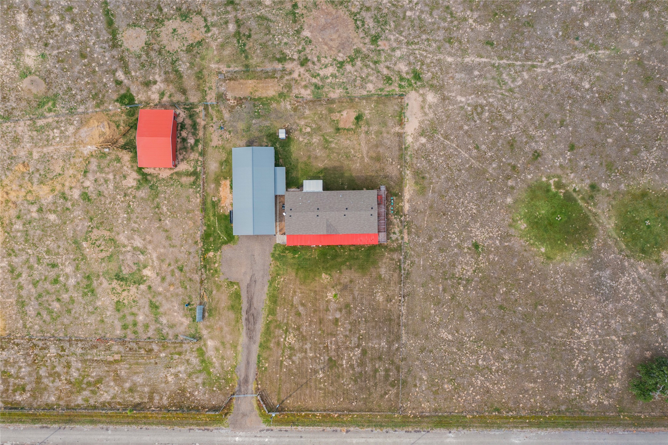 664 Garrett Road Yoakum, TX 77995 - Photo 26 of 39 Aerial property overview featuring a main structure with a gray shingle roof and red accents, a secondary structure with a light blue metal roof, and a separate red outbuilding