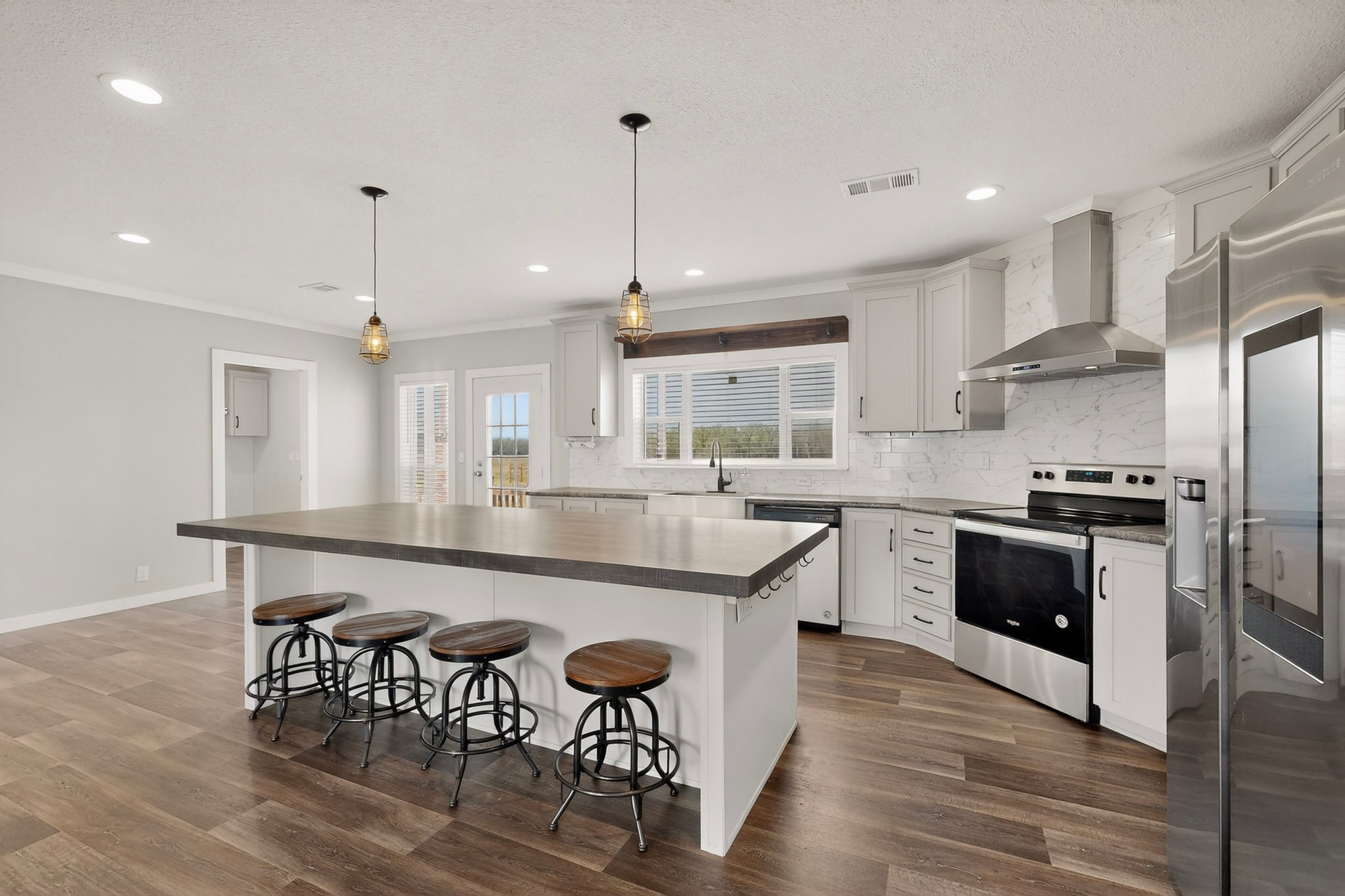 664 Garrett Road Yoakum, TX 77995 - Photo 32 of 39 Open-concept kitchen featuring a large central island, Beauflor luxury vinyl plank flooring, white cabinetry, integrated stainless steel appliances, and a tile backsplash