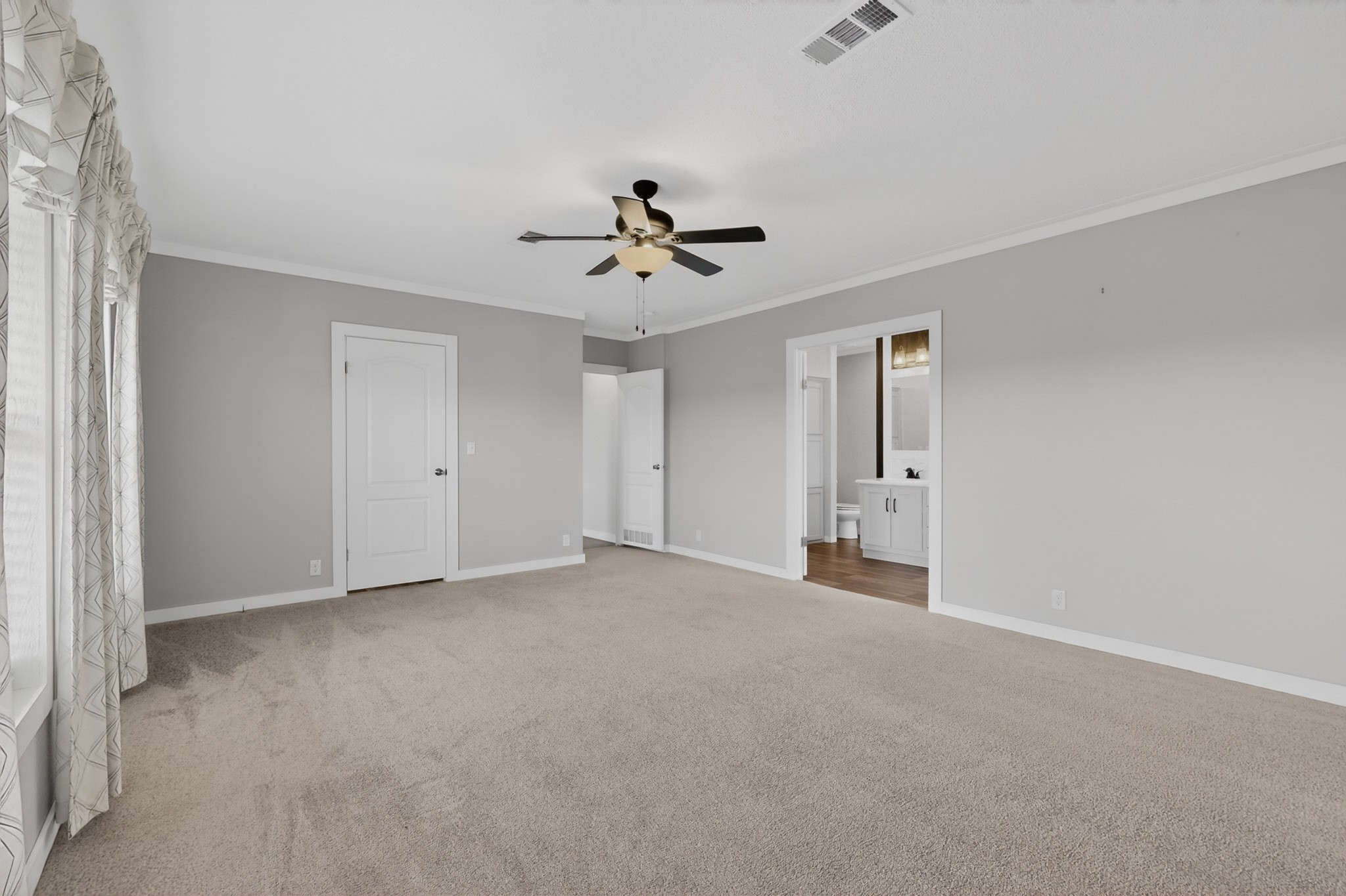 664 Garrett Road Yoakum, TX 77995 - Photo 33 of 39 Spacious carpeted room featuring light gray walls, white trim, a ceiling fan with light fixture, and a doorway leading to a bathroom