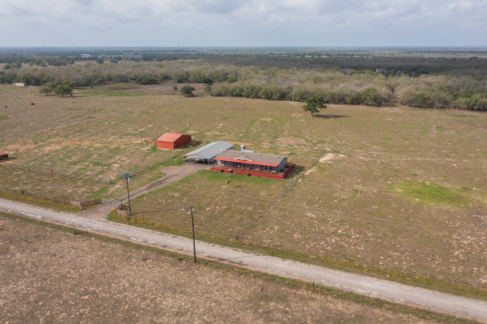 664 Garrett Road Yoakum, TX 77995 - Photo 39 of 39 Expansive rural property featuring a primary residence with a red exterior, a red barn, and a covered carport structure, all set within open fields with scattered trees