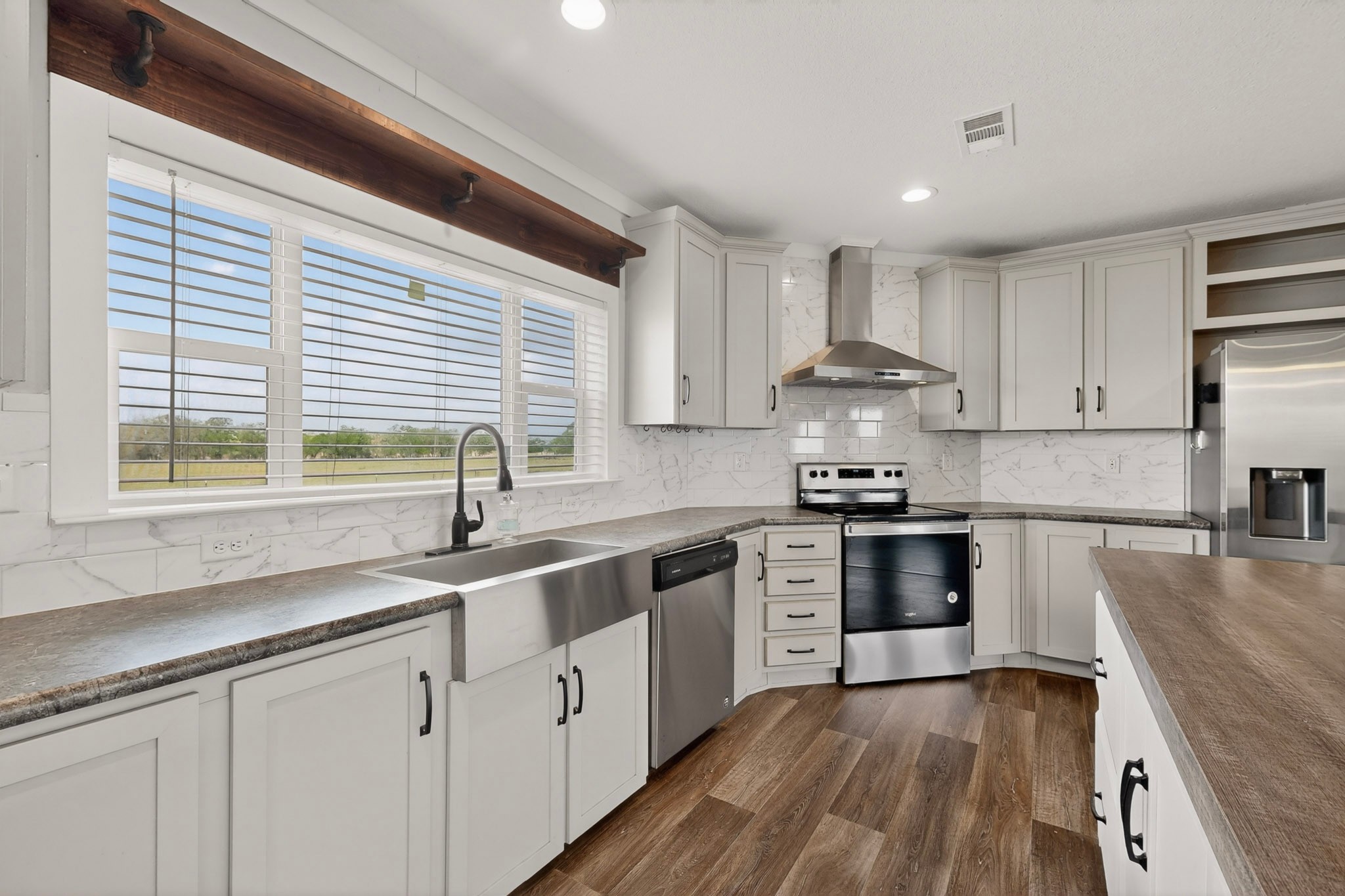 664 Garrett Road Yoakum, TX 77995 - Photo 5 of 39 Kitchen featuring white shaker-style cabinetry, stainless steel appliances, a farmhouse sink with a gooseneck faucet, and a stone-look backsplash
