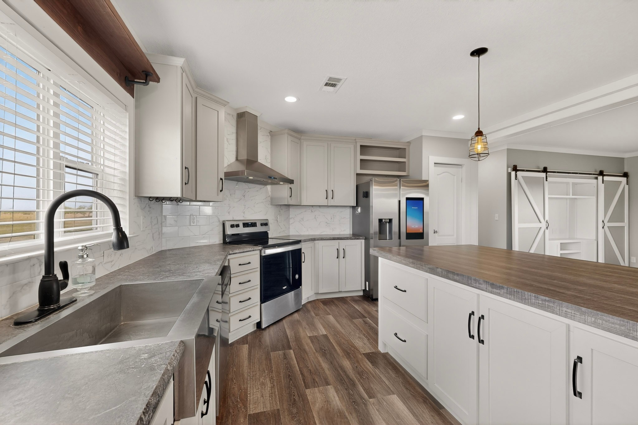 664 Garrett Road Yoakum, TX 77995 - Photo 6 of 39 Modern kitchen featuring white cabinetry, stainless steel appliances, a large center island with a wood-finish countertop, Beauflor luxury vinyl plank flooring and a white tile backsplash