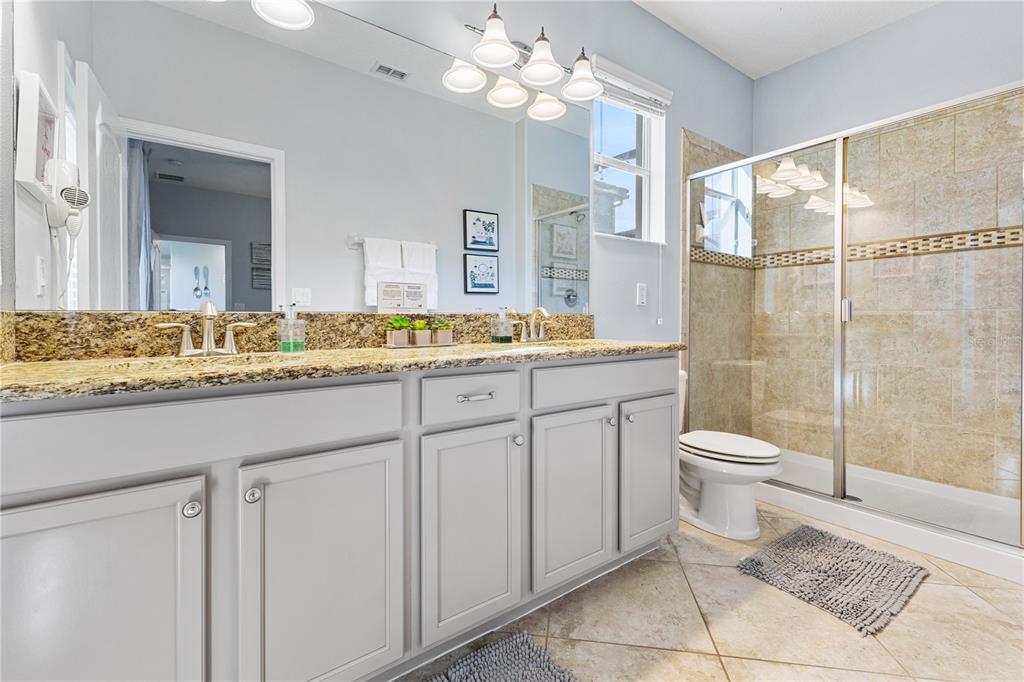 9006 Majesty Palm Road Kissimmee, FL 34747 - Photo 26 of 56 a bathroom with a granite countertop sink toilet a mirror and a shower
