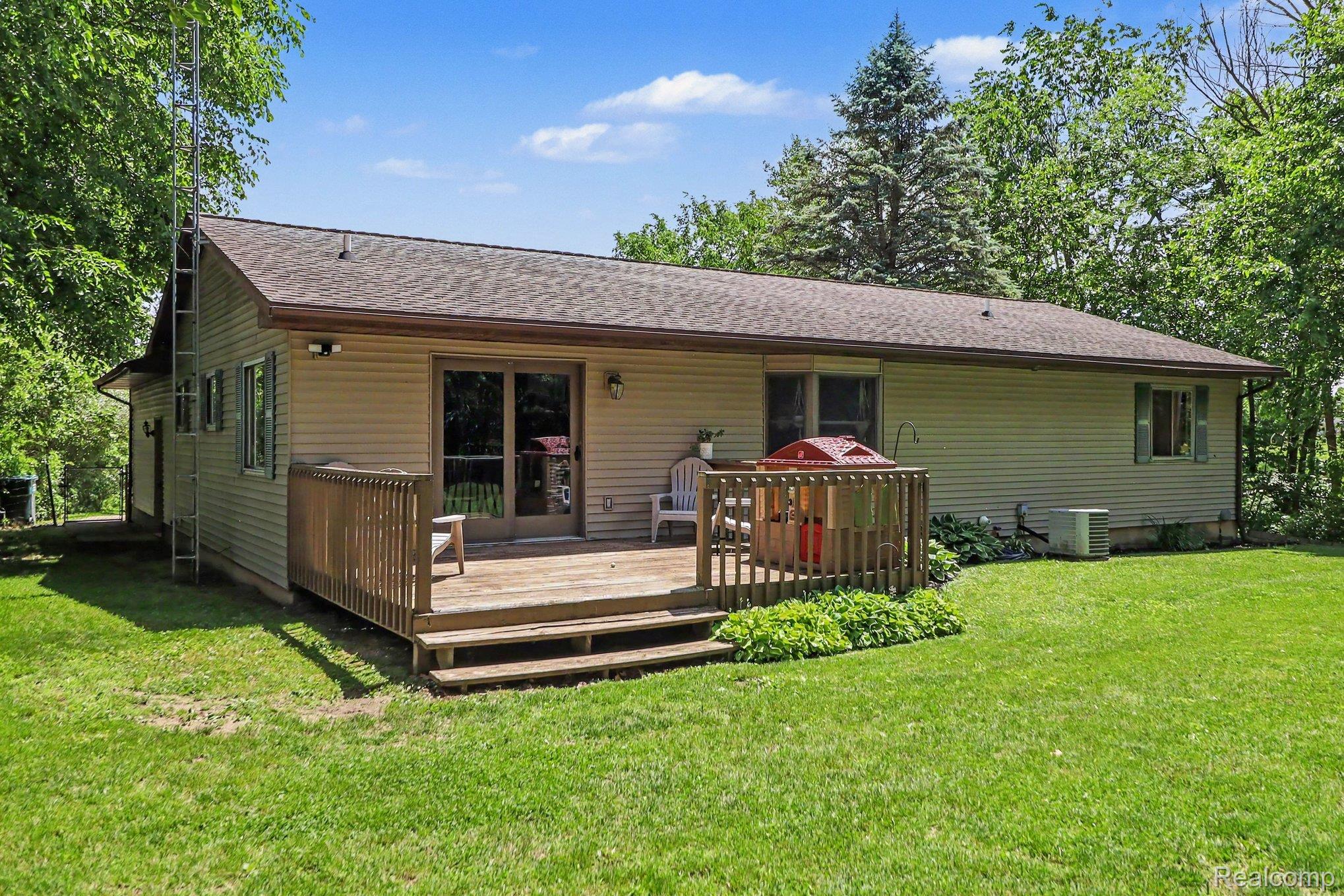 2905 German Road Columbiaville, MI 48421 - Photo 4 of 31 Rear exterior featuring a wood deck with steps, sliding glass patio doors, beige siding, and a gabled roofline