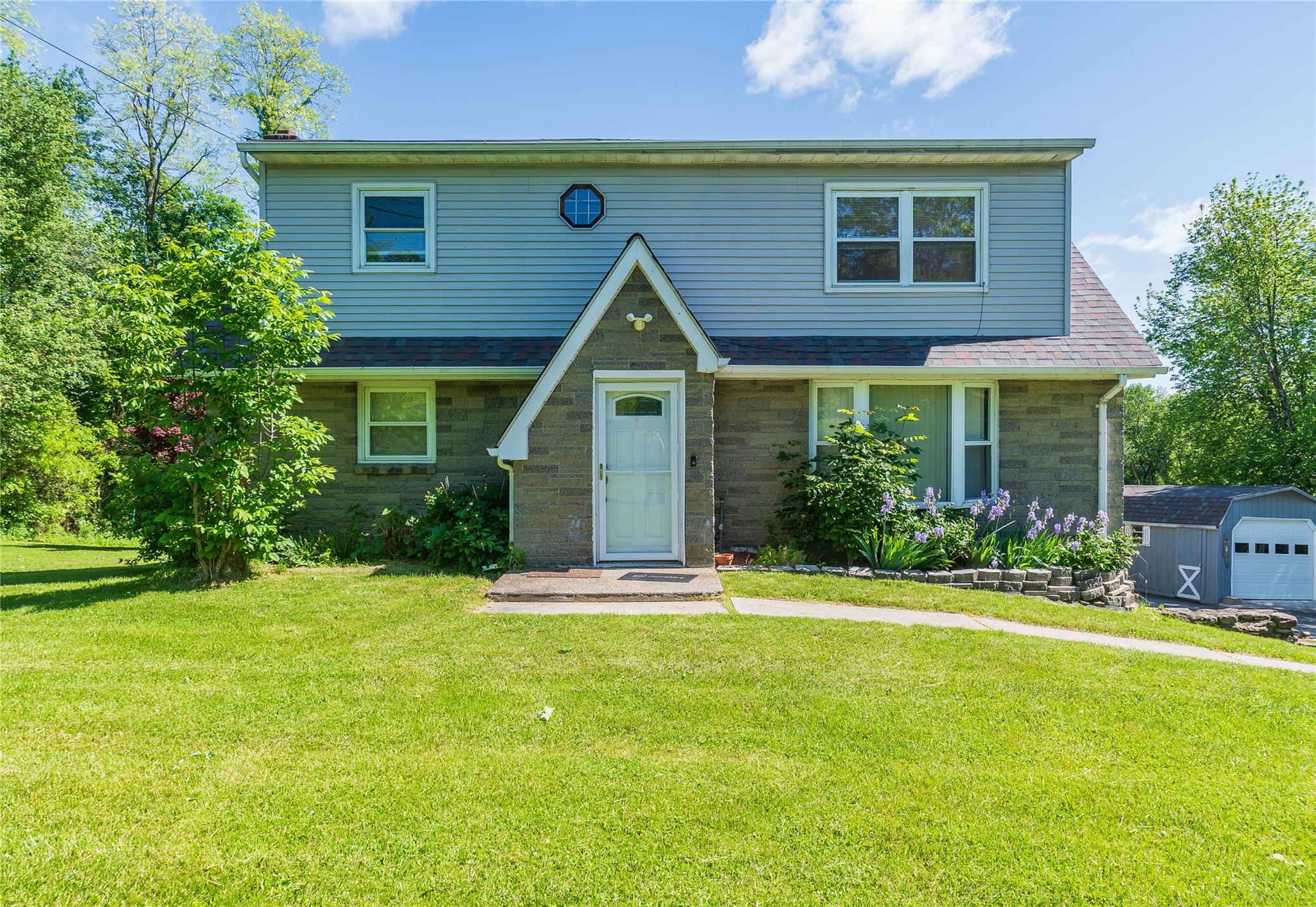 View of front facade featuring stone siding, a front yard, and an outdoor structure
