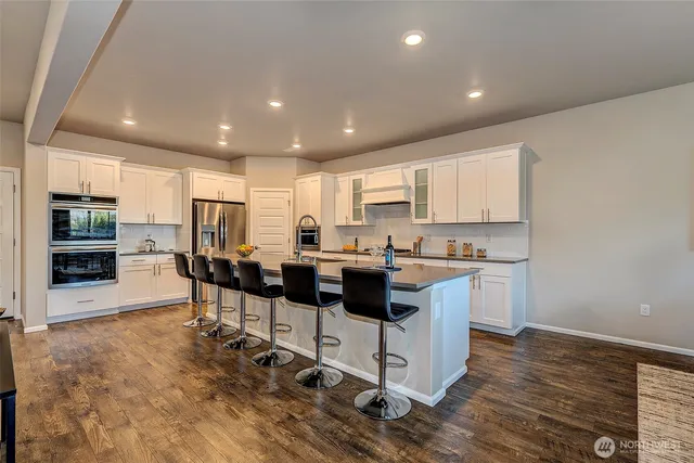 a kitchen with stainless steel appliances kitchen island granite countertop a stove a sink a refrigerator and white cabinets with wooden floor