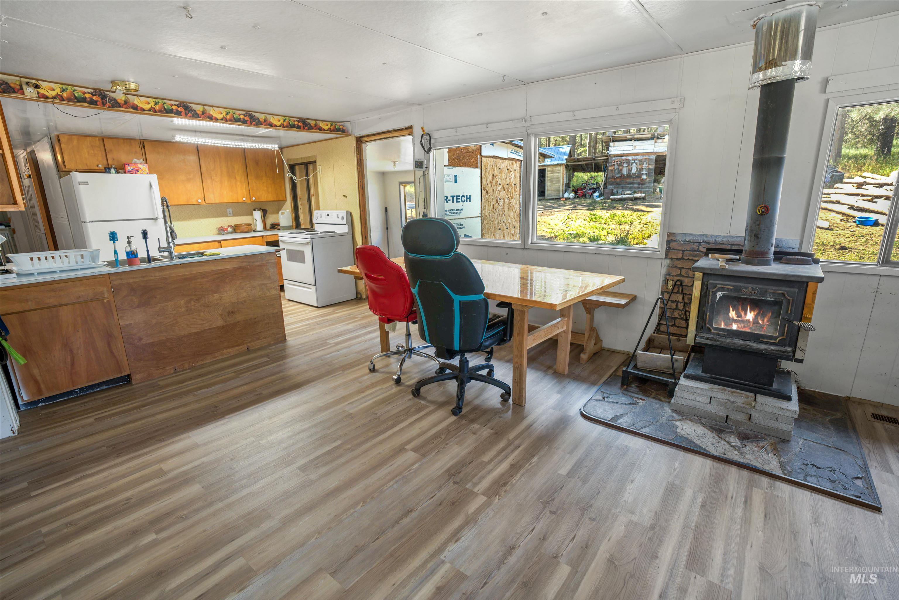 1910 East Mountain Road Anatone, WA 99401 - Photo 12 of 41 Wood-finish flooring, wood-burning stove with stone hearth, multiple windows, built-in cabinetry, and white appliances