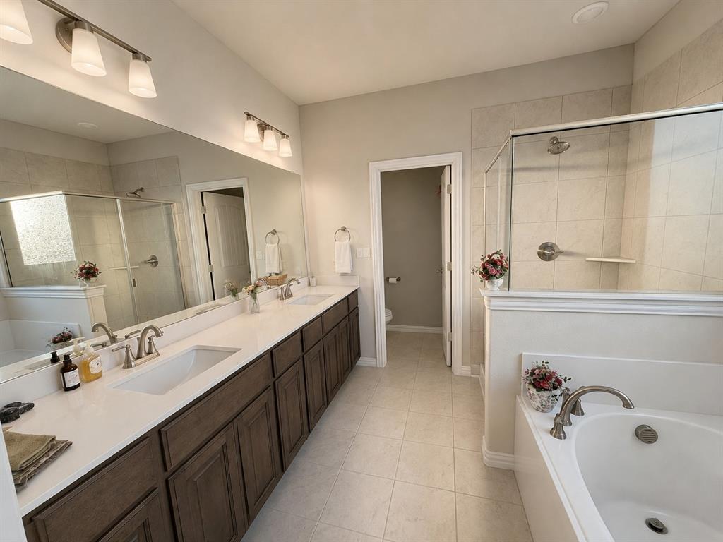 131 Llanos Drive Decatur, TX 76234 - Photo 7 of 9 Spacious bathroom featuring a dual vanity with wood-finish cabinetry and white countertops, a walk-in shower with glass enclosure and tiled walls, a separate built-in soaking tub, and tile flooring