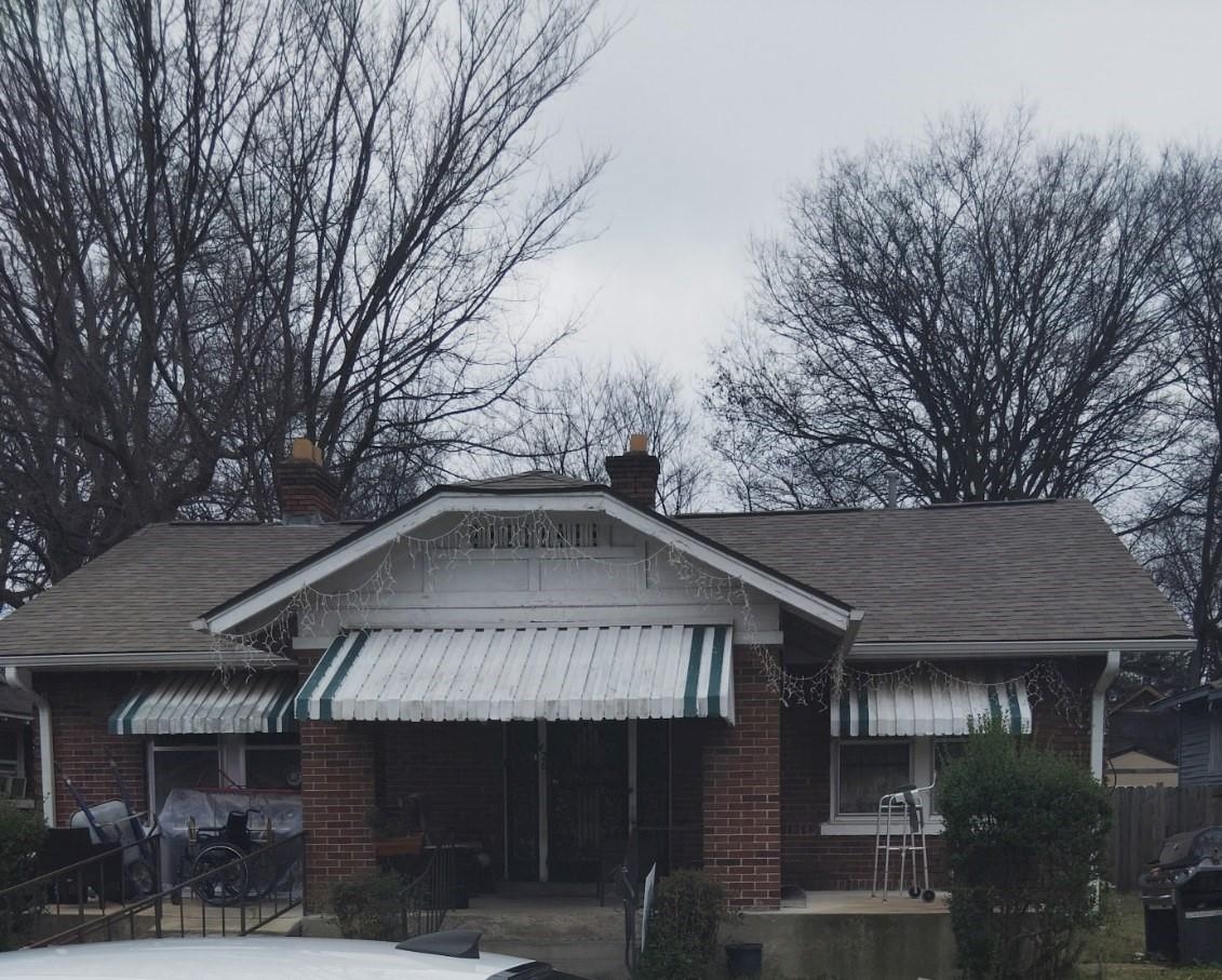 Bungalow featuring brick siding, a chimney, and a shingled roof