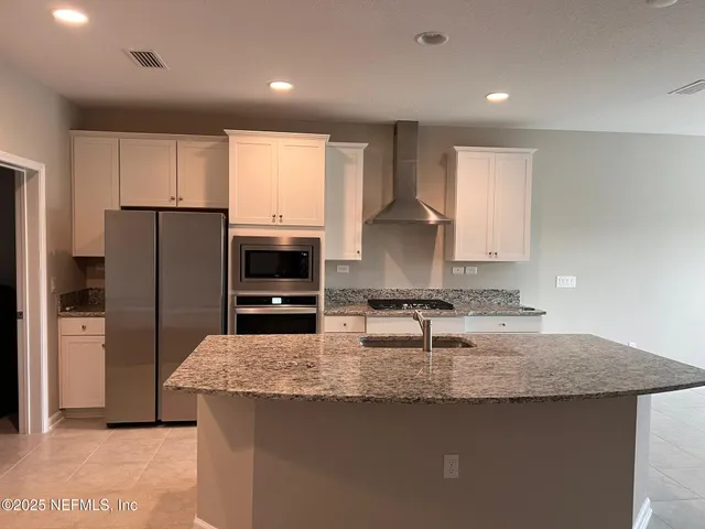 a kitchen with granite countertop a refrigerator a sink a stove a microwave a counter top and cabinets