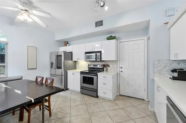 a kitchen with stainless steel appliances a stove a sink dishwasher a refrigerator with a dining table and chairs