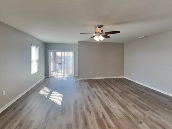 an empty room with wooden floor chandelier fan and windows