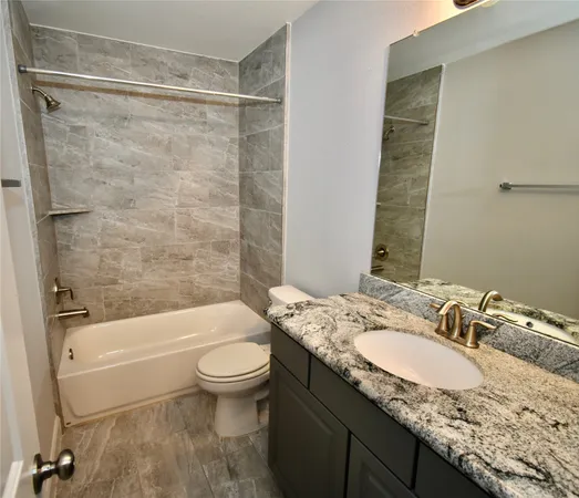 a bathroom with a granite countertop sink a toilet and shower