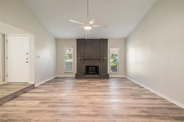 a view of an empty room with wooden floor fireplace and a window