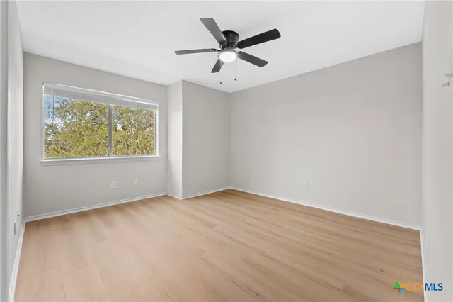 an empty room with wooden floor ceiling fan and windows