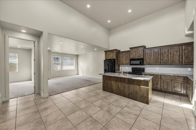 794 North Via Modelo Circle Washington, UT 84780 - Photo 7 of 21 Kitchen with light tile patterned floors, an island with sink, light stone countertops, light colored carpet, and black appliances