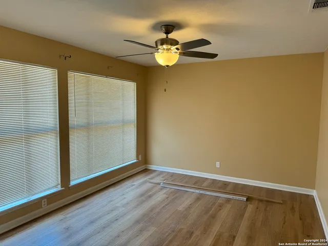 an empty room with wooden floor fan and windows