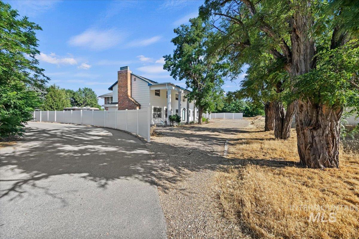 2160 South Five Mile Road Boise, ID 83709 - Photo 5 of 41 Long paved driveway leading to a white residence with a prominent brick chimney
