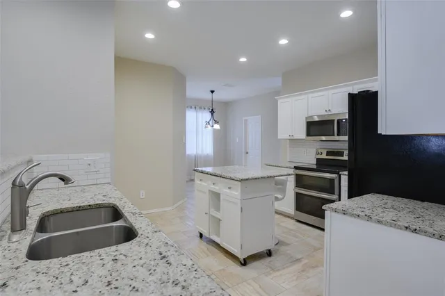 a kitchen with granite countertop a sink stainless steel appliances and white cabinets