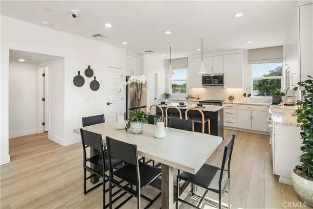 a kitchen with stainless steel appliances kitchen island granite countertop a dining table chairs and a refrigerator